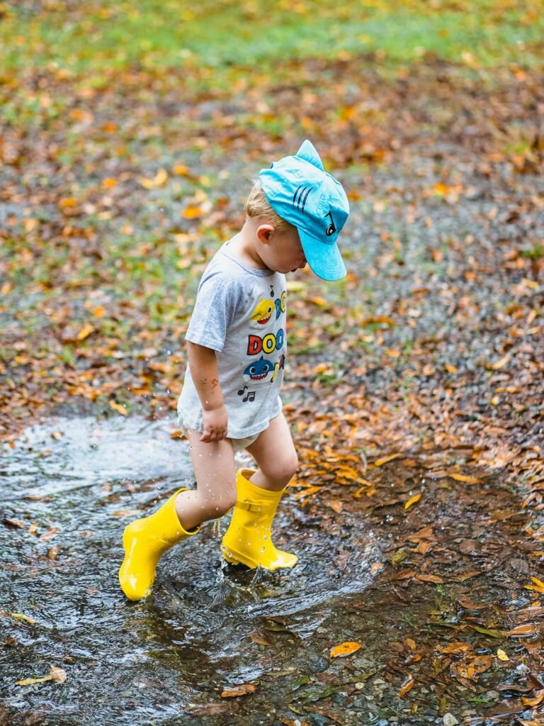 Toddler in yellow rain boots splashing in a puddle, a typical fall day in Bremerton with toddlers